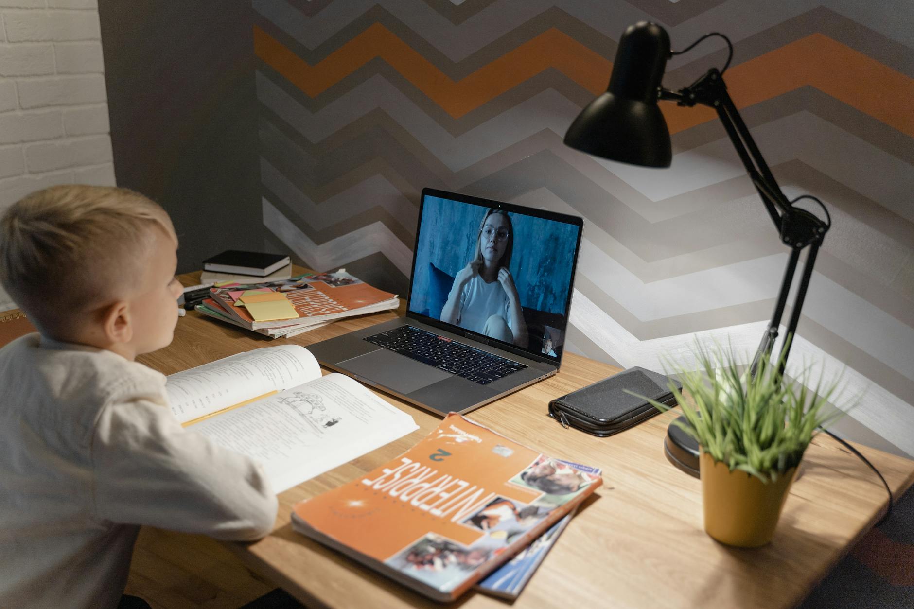 A student engaging in online education at home with a laptop and study materials. — education debate