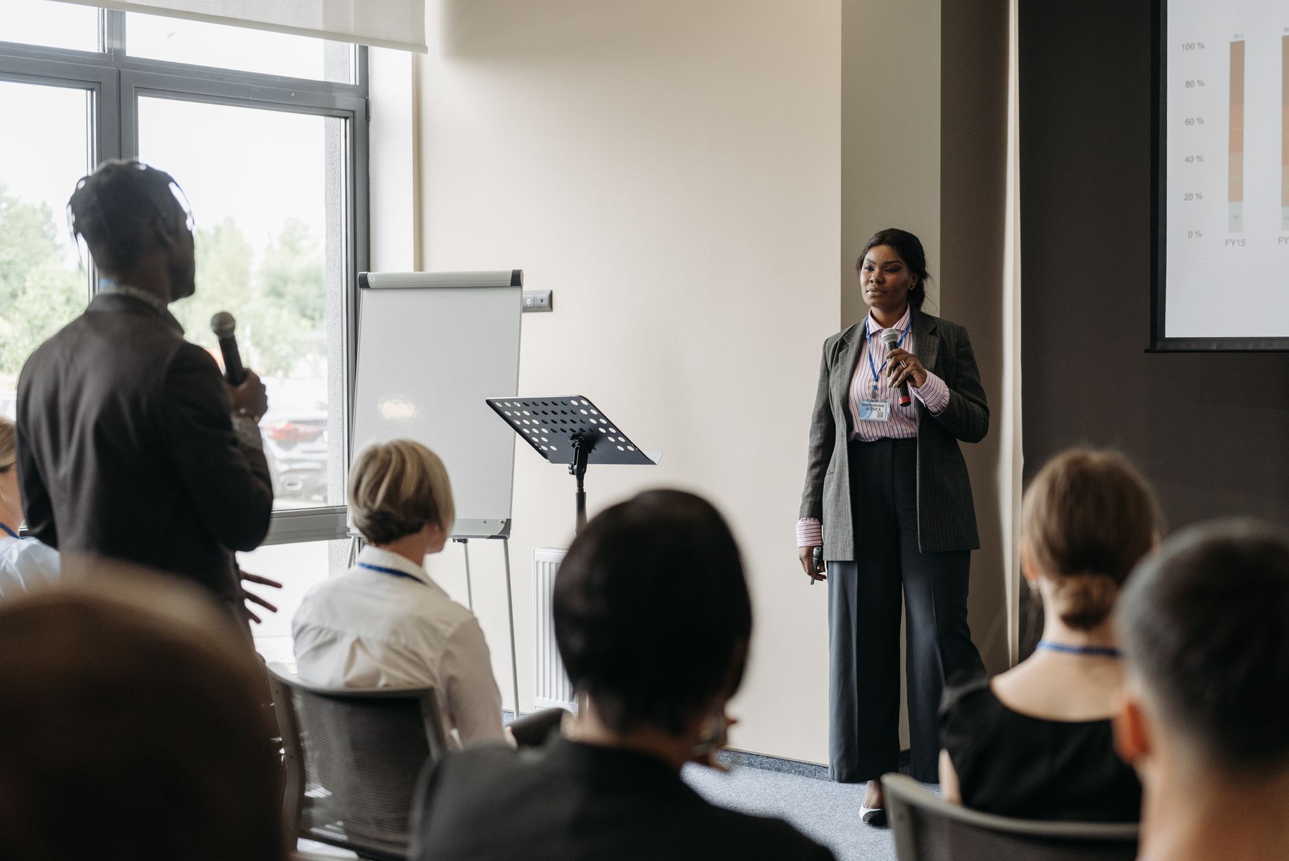 A moderator standing in front of participants, holding a notepad and ensuring a fair discussion. — hosting debates