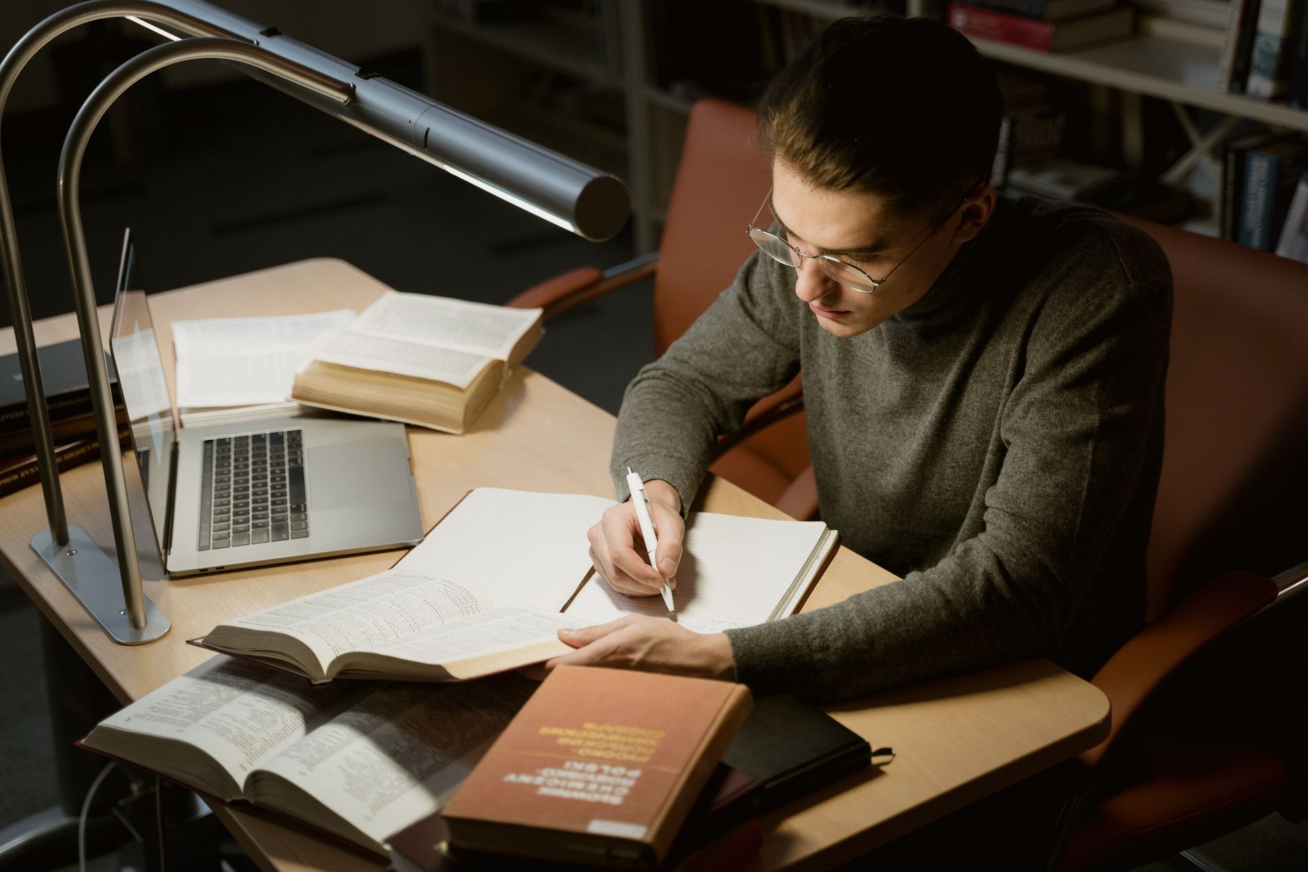 A student researching debate topics with books and a laptop, illustrating the importance of thorough research in debate preparation.