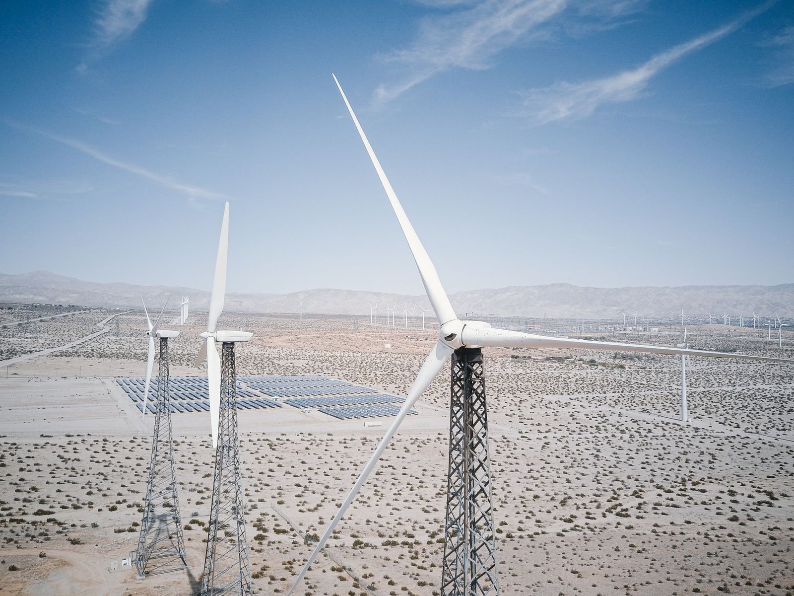 A photo of a modern solar farm with wind turbines in the background. — renewable energy debate