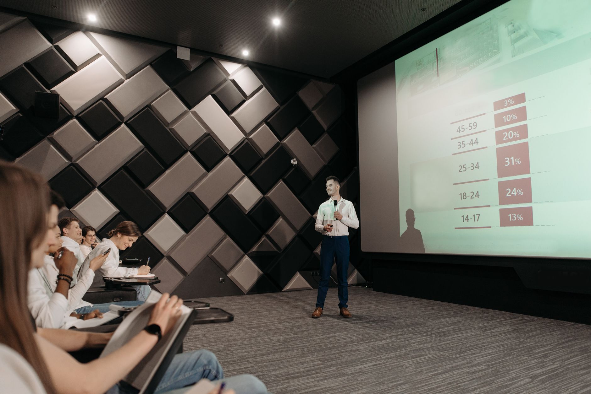 A speaker engaging with an audience during a debate with visual aids in the background. — audience engagement in debates