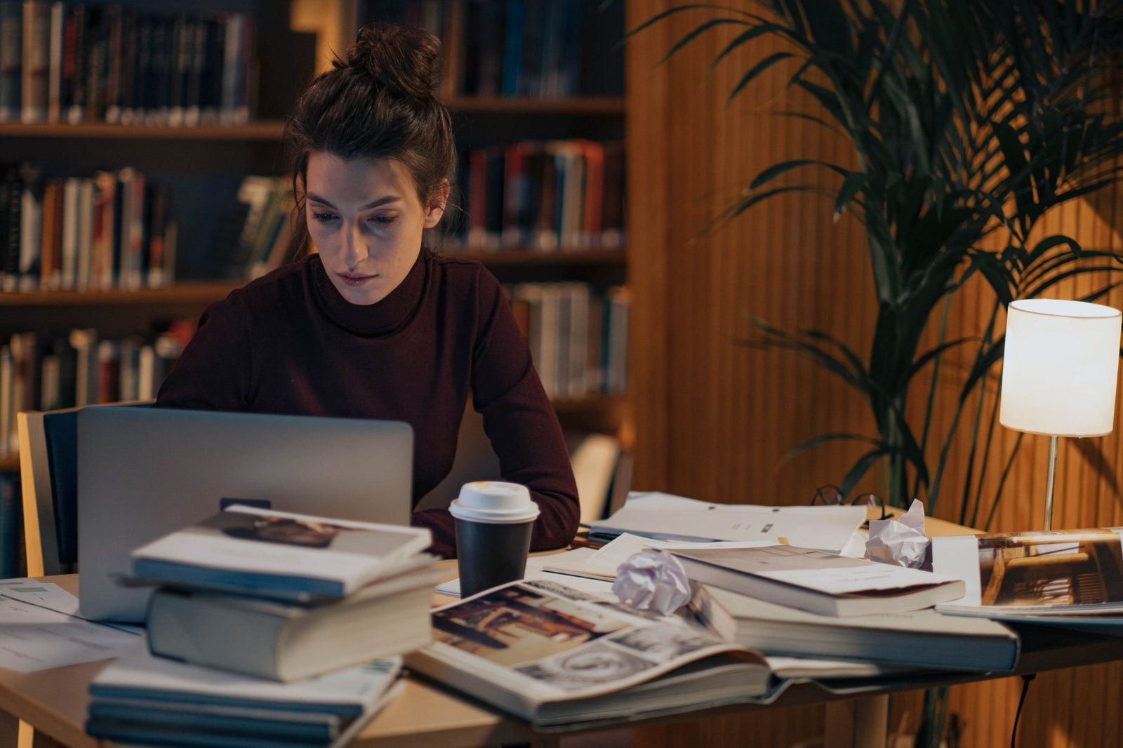 A focused student researching debate topics with books and a laptop. — debate preparation