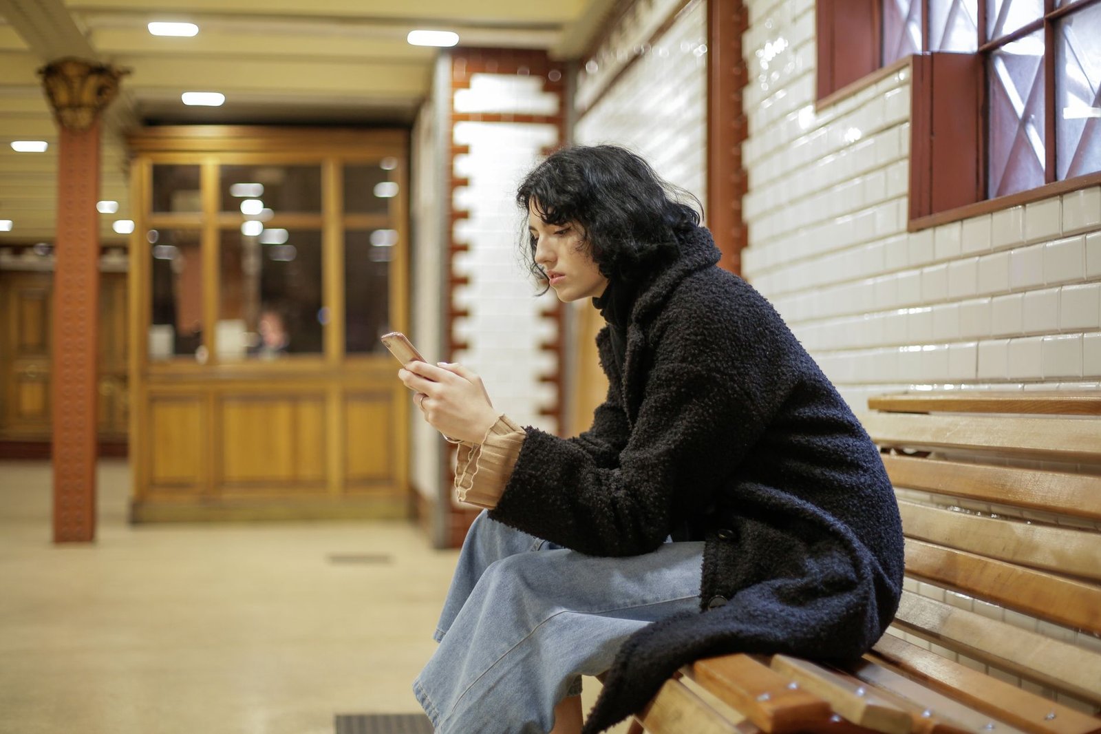 A person sitting alone in a crowded place, looking at their phone, illustrating technology isolation.