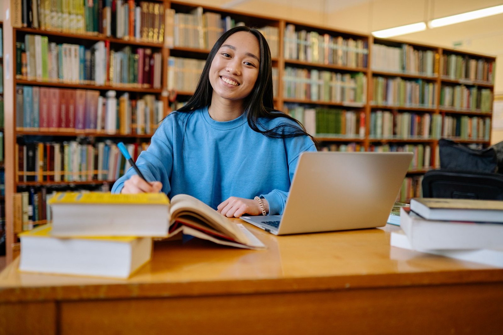 A student researching debate topics with books and a laptop, symbolizing effective debate preparation.