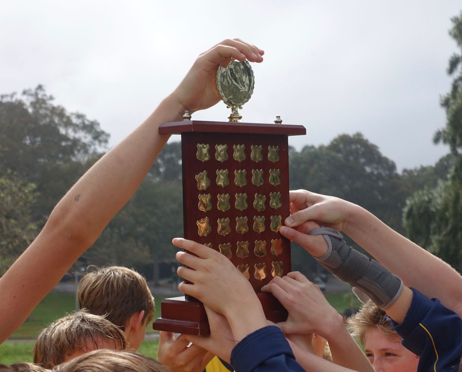 A close-up of a debate trophy with participants celebrating in the background. — debate club benefits